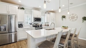 A modern kitchen with white cabinetry, stainless steel appliances, and a central island with bar stools. - NEW LISTING! Lost Key Golf & Beach Club~ Happy Ours -  NO HASSLE CHECK OUT (Pensacola)