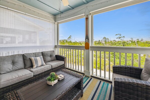 A covered porch with a gray sofa, wicker chairs, a wooden table with plants, and a view of greenery. - NEW LISTING! Lost Key Golf & Beach Club~ Happy Ours - NO HASSLE CHECK OUT (Pensacola)