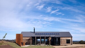 A modern house with a sloped roof, solar panels, and large windows. - HILLPLAINS HOUSE - 100% OFF GRID LUXURY (Metcalfe)
