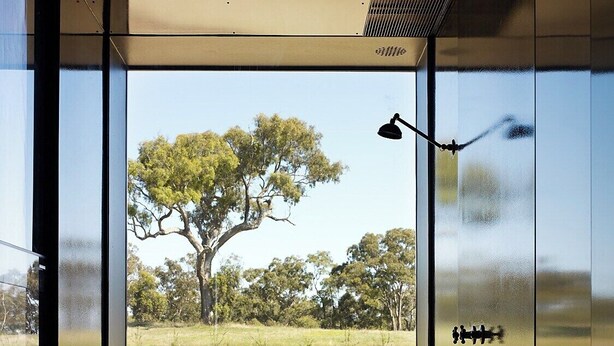 A modern interior with large glass windows, a metal desk, and a view of a tree and open field. - HILLPLAINS HOUSE - 100% OFF GRID LUXURY (Metcalfe)