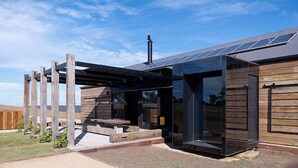 A modern house with a wooden exterior, a covered patio, and solar panels on the roof. - HILLPLAINS HOUSE - 100% OFF GRID LUXURY (Metcalfe)