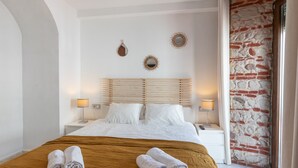 Een hotelkamer met een bed, twee nachtkastjes, een hoofdeinde en een bakstenen muur.