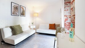 Een moderne woonkamer met een witte bank, een klein bijzettafeltje met een fles en glazen, en een vloerlamp.