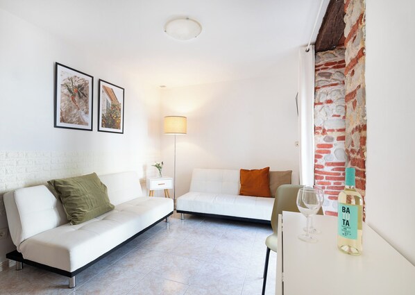 Ein modernes Wohnzimmer mit einem weißen Sofa, einem kleinen Beistelltisch mit Flasche und Gläsern sowie einer Stehlampe.
