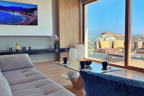 A modern living room with a sofa, a glass coffee table, and a view of a coastal cityscape through large windows. - Villa with private swimming pool (Cullera)