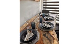 Een eettafel gedekt met borden, bestek en glazen, met een houten tafel en een raam op de achtergrond.