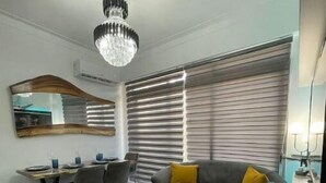 Een moderne woonkamer met een eetgedeelte, een kroonluchter, een grote spiegel en een bank met een geel kussen.