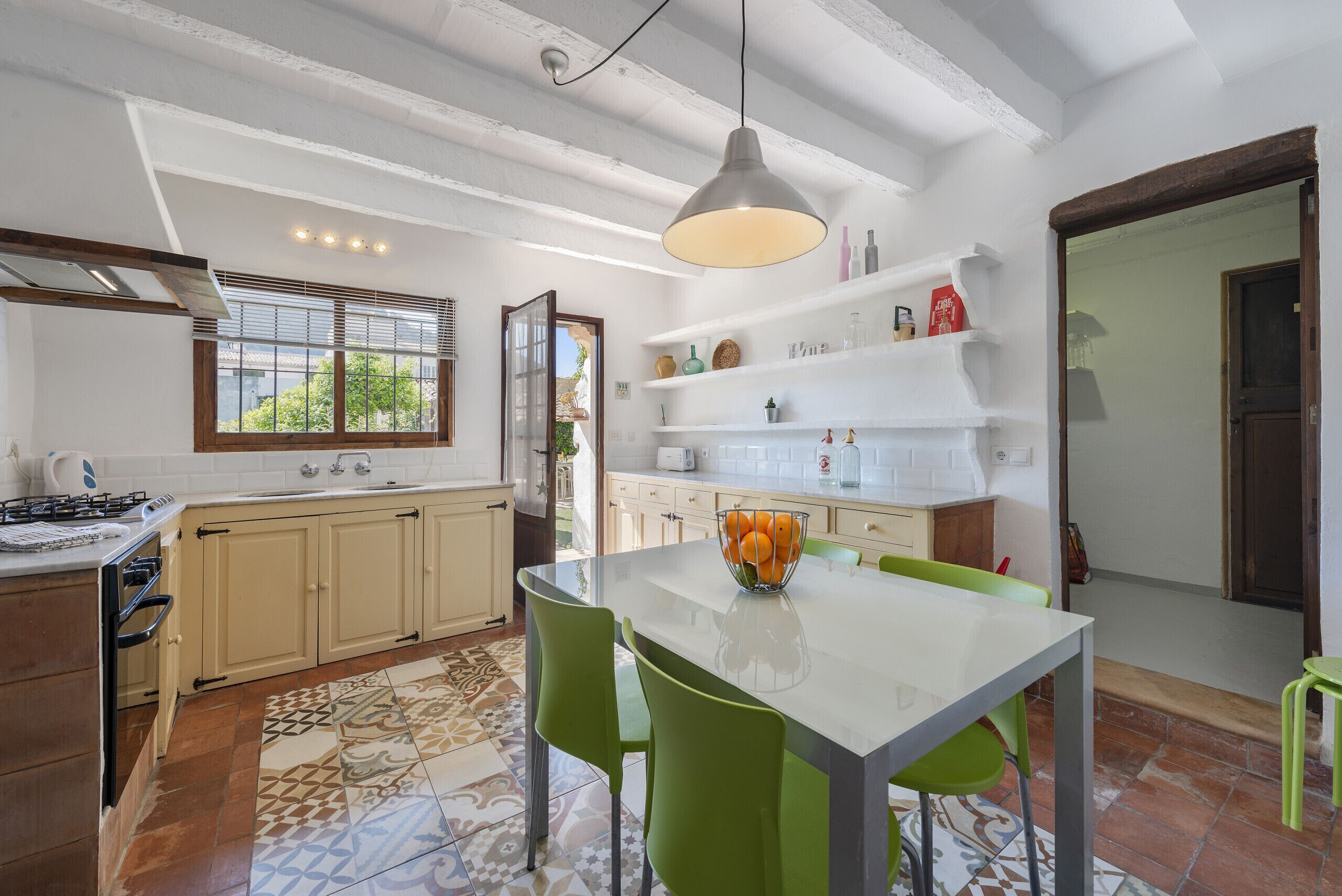 A kitchen with a dining table, chairs, a hanging light fixture, and a window with blinds.