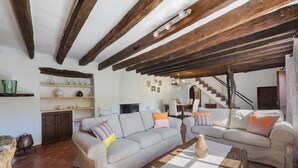 A spacious living room with exposed wooden beams, a sofa set, a coffee table, and a fireplace. - Es Garroverar Villa: Luxurious Retreat in the Heart of Majorca (Pollensa)