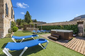 A courtyard with lounge chairs, a hot tub, and a wooden deck. - Es Garroverar Villa: Luxurious Retreat in the Heart of Majorca (Pollensa)
