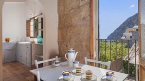 A dining area with a table set for four, a kitchen in the background, and a view of a mountainous landscape through a balcony. - Es Garroverar Villa: Luxurious Retreat in the Heart of Majorca (Pollensa)