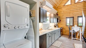 A modern kitchen with a built-in washer and dryer, wooden walls, and a dining area with a table and chairs. - Secluded Grand Junction Getaway w/ Sweeping Views! (Grand Junction)