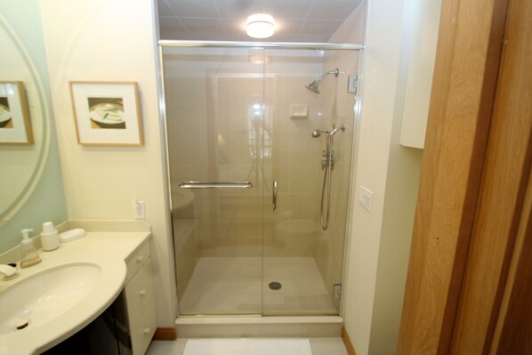 Een moderne badkamer met een glazen douchecabine, een witte wastafel en een spiegel.