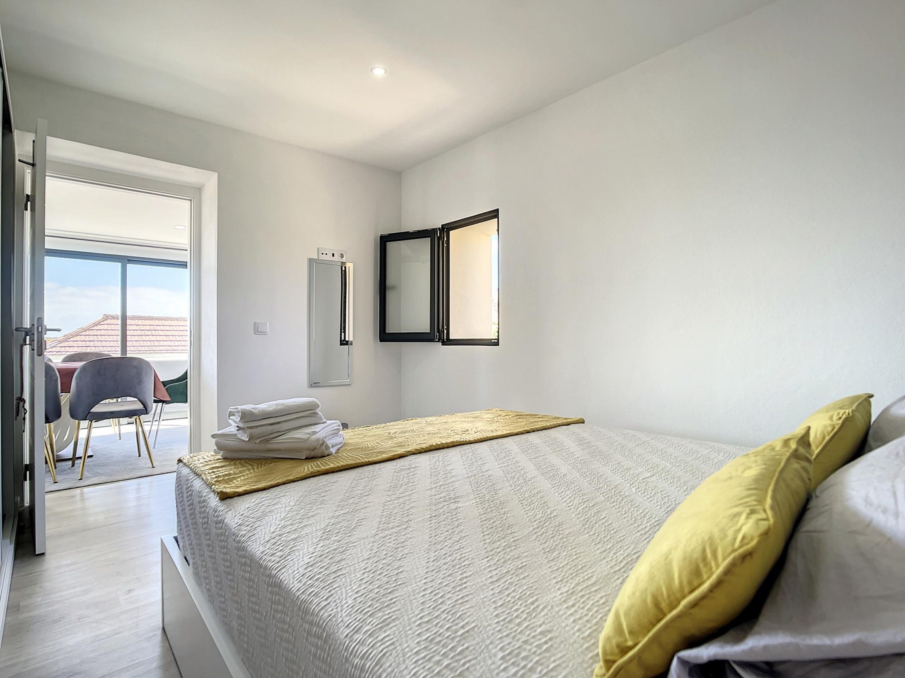 A bedroom with a bed, a bedside table, a mirror, and a view of the outside.