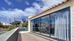 Un balcón con suelo de madera, puerta de cristal y vista a una montaña y casas al fondo.
