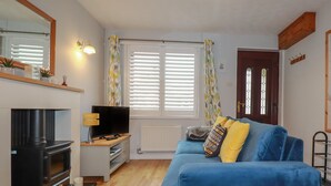 A living room with a fireplace, a sofa, a television, and a window with blinds. - Bumbles (Padstow)