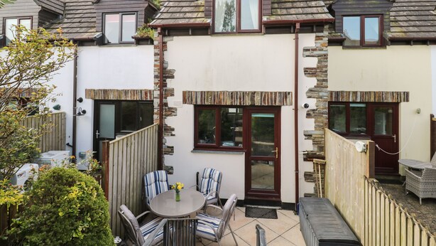 A house with a stone facade, a wooden roof, and a small patio with a table and chairs. - Bumbles (Padstow)