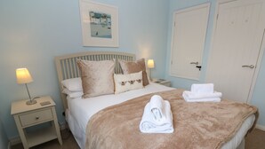 A bedroom with a bed, two bedside tables, a nightstand, a framed picture on the wall, and a door. - Bumbles (Padstow)