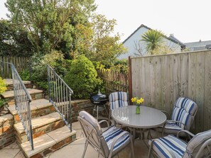 A patio with a round table and striped chairs, surrounded by a wooden fence and a stone staircase. - Bumbles (Padstow)