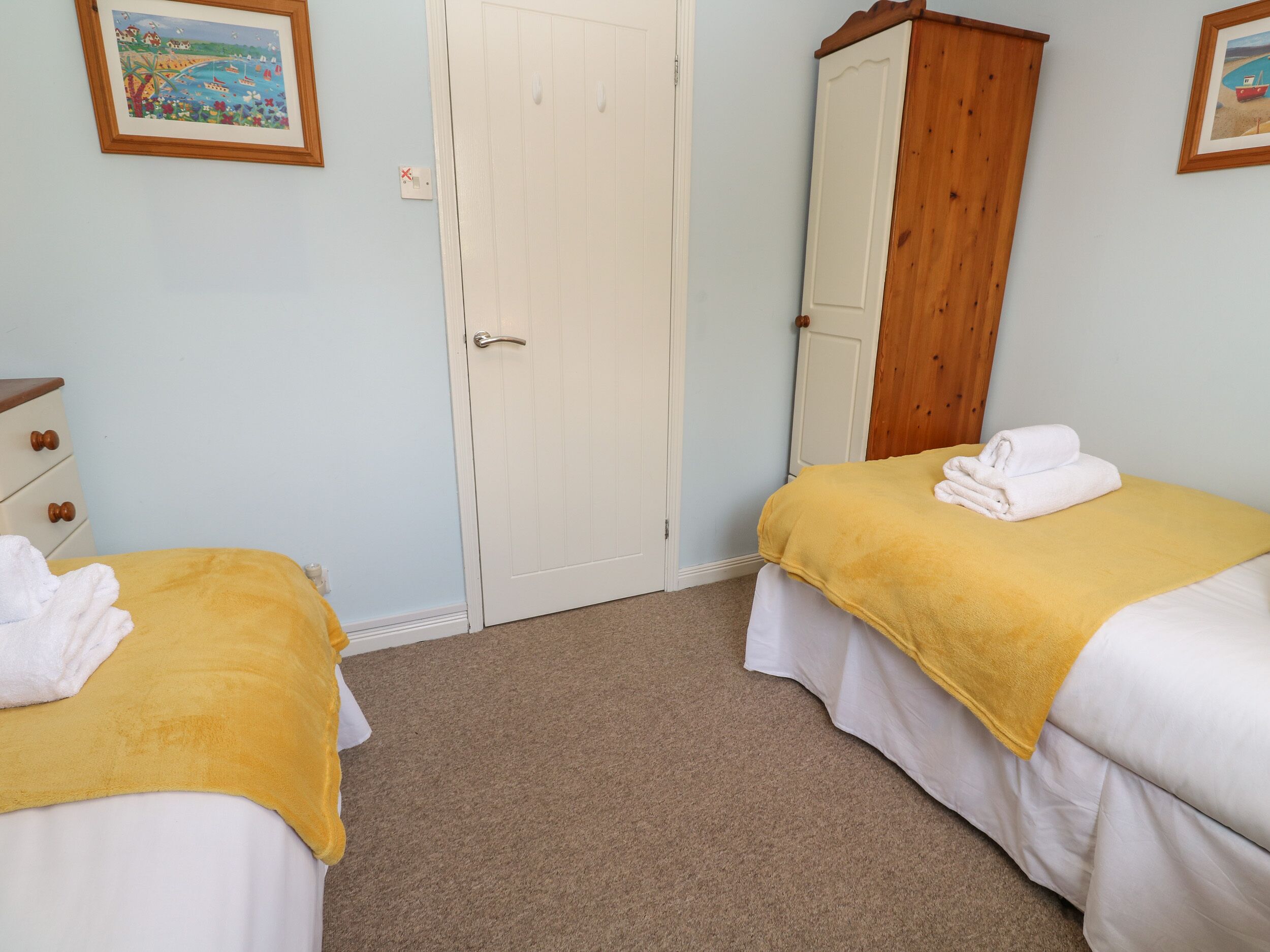 A bedroom with two beds, a wooden wardrobe, and a door.