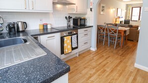 A modern kitchen with white cabinets, a black granite countertop, and a wooden dining area with a table and chairs. - Bumbles (Padstow)