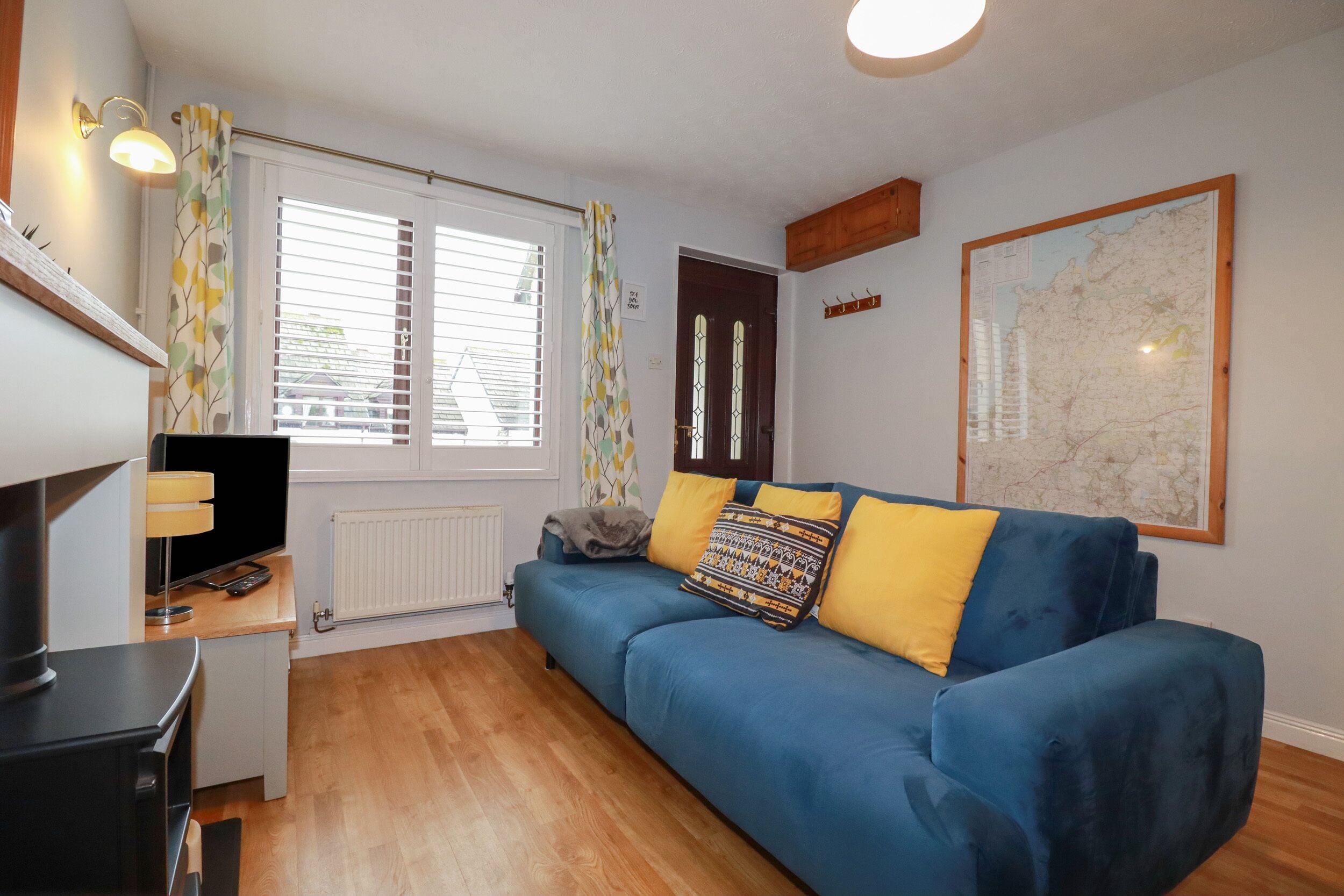 A compact living space with a blue sofa, a small desk with a lamp, a radiator, and a map on the wall.