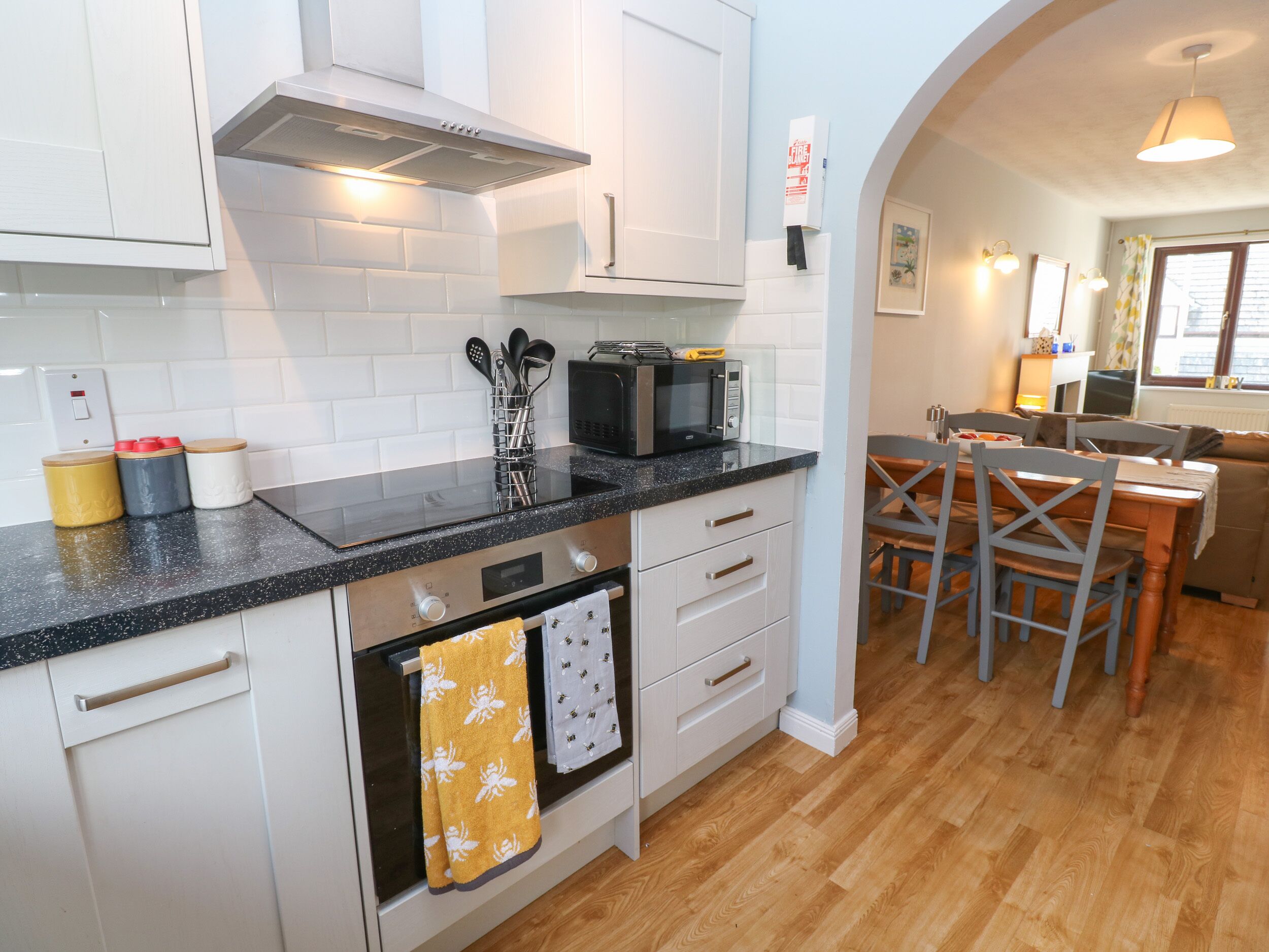 A modern kitchen with white cabinets, a black countertop, and a microwave. There is a dining area with a table and chairs visible through an archway.