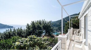 Enjoy the serene coastal view from this balcony, featuring a seating area with a railing and lush surroundings.