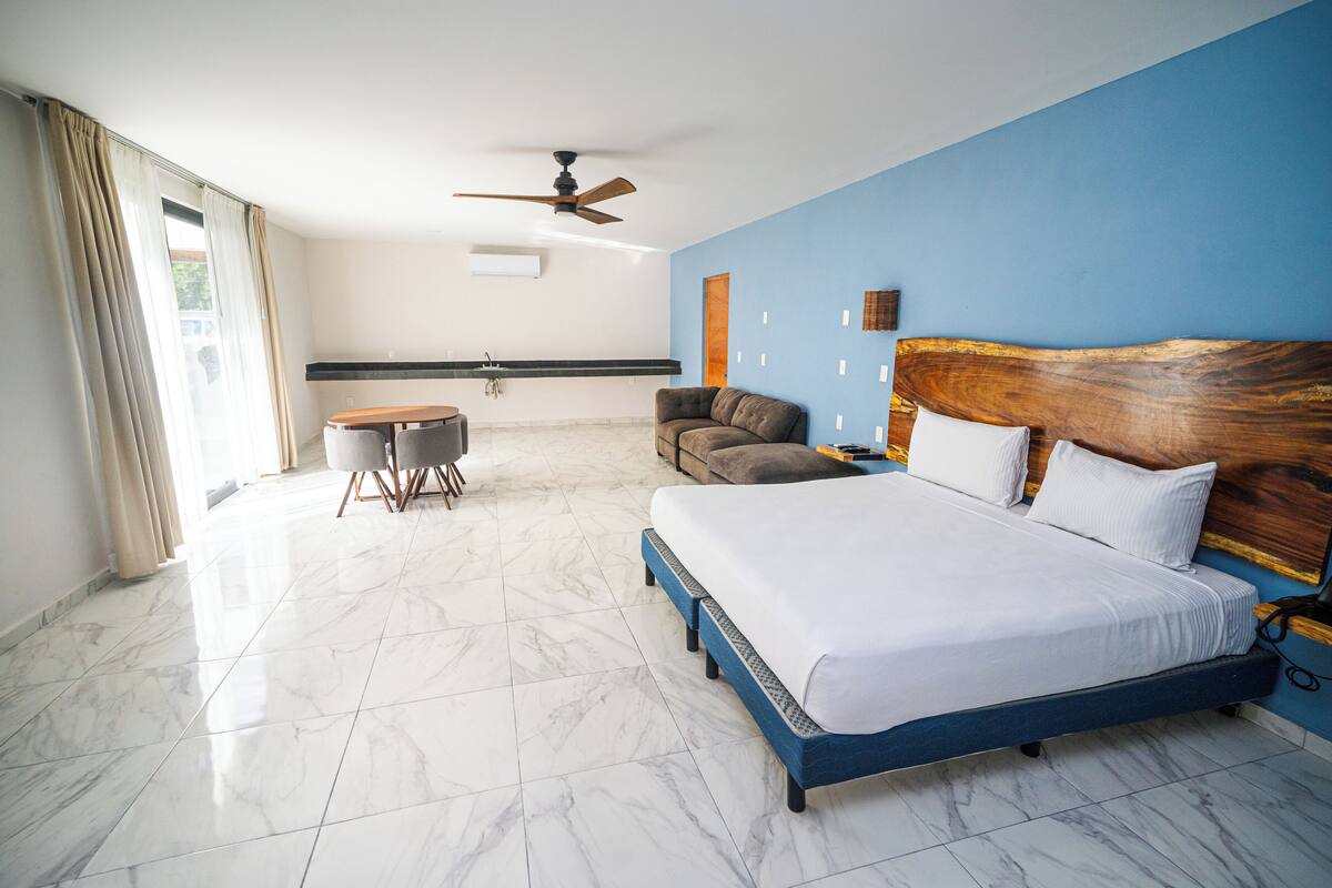 A hotel room with a large bed, a ceiling fan, a dining table, and a sofa.