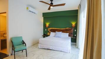 Habitación de hotel con cama, una silla, ventilador de techo y aire acondicionado instalado en la pared.