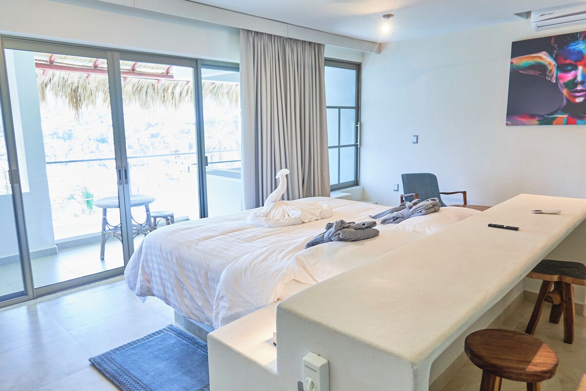 Ett hotellrum med en stor säng, ett skrivbord och en stol. Det finns ett fönster med gardiner och utsikt över omgivningen.