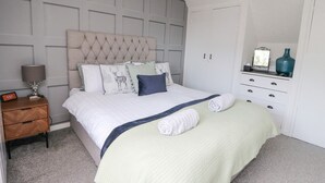 A bedroom with a tufted headboard, a bed with a quilted cover, a nightstand with a lamp, a dresser with drawers, and a mirror on the dresser. - Ben View (Arrochar)