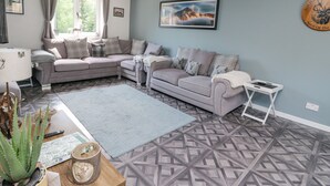 A living room with a sectional sofa, a small table, a blue rug, and a patterned floor. - Ben View (Arrochar)