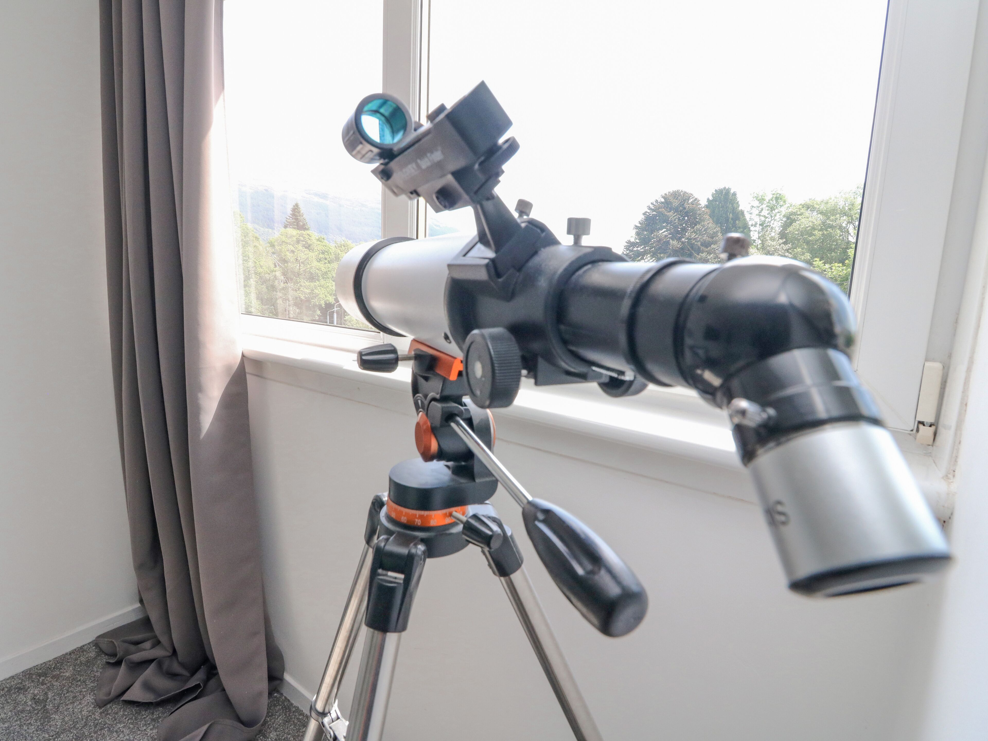 A telescope on a tripod near a window with curtains.