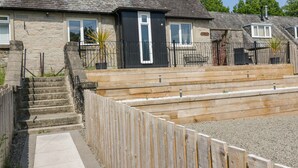 A two-story house with a stone facade, a black front door, and a small front yard with wooden steps leading to the entrance. - Ben View (Arrochar)