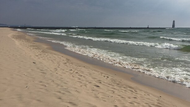 A beach with a lighthouse in the distance, sandy shore, and waves approaching. - Beachside Apt 2 (Frankfort)