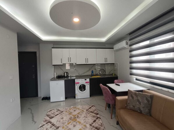 Un espacio habitable compacto con kitchenette, lavadora, comedor y sofá.