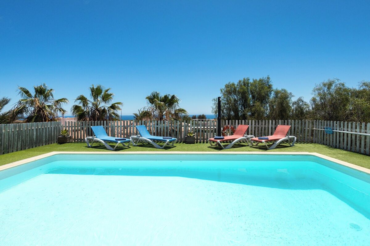Una piscina rectangular con agua cristalina azul, rodeada por una valla de madera.