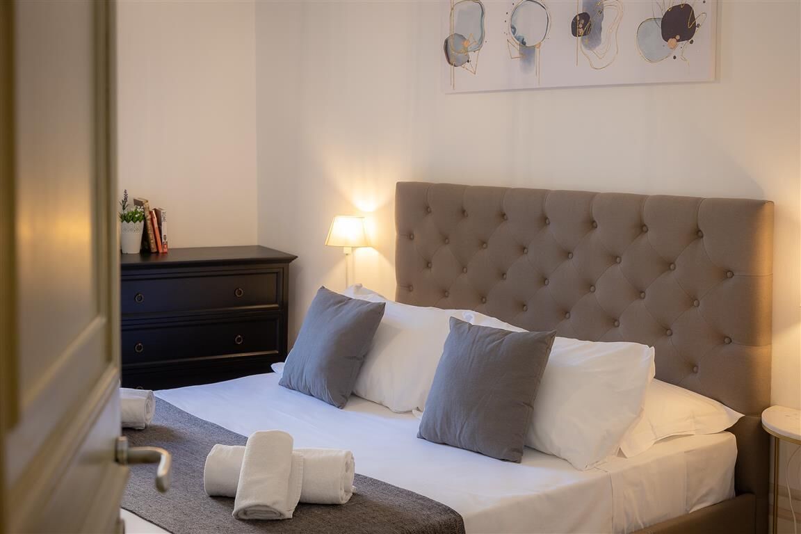 A neatly made bed with a tufted headboard, a bedside table with a lamp, and a wall with abstract art.