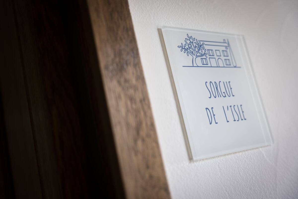 A sign with a tree and building illustration and the text "SORGUE DE L'ISLE".