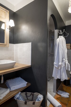 Un baño moderno con un lavamanos grande blanco, un estante de madera con toallas, un tapete de baño blanco y una zona de ducha con puerta de vidrio.