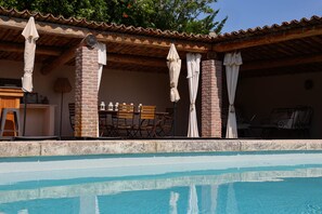 Zona de piscina con una estructura de ladrillo, mobiliario exterior y sombrillas.