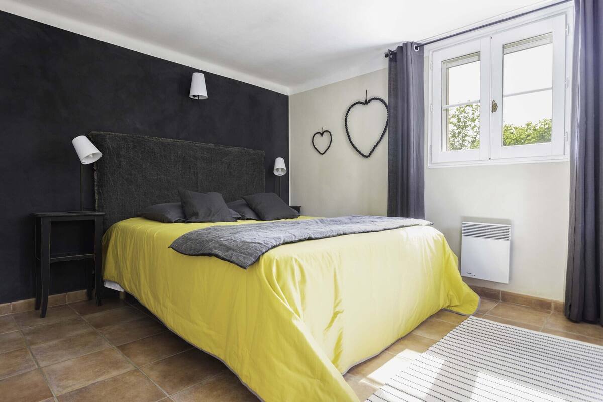A bedroom with a bed, two bedside tables, a window, and a wall-mounted heater.