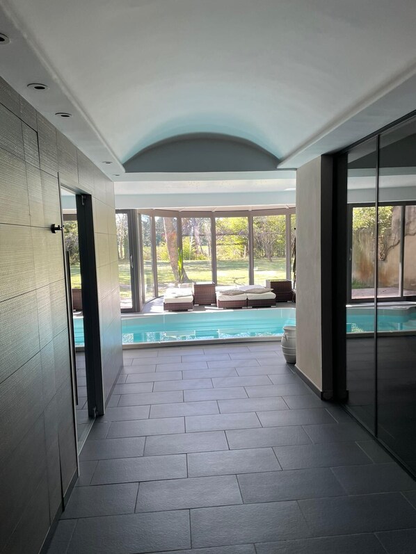 A modern interior with a pool area, featuring a glass-enclosed patio and a view of the outdoors. - DOMAINE DU MOULIN DE VILLEFRANCHE (Pernes-les-Fontaines)