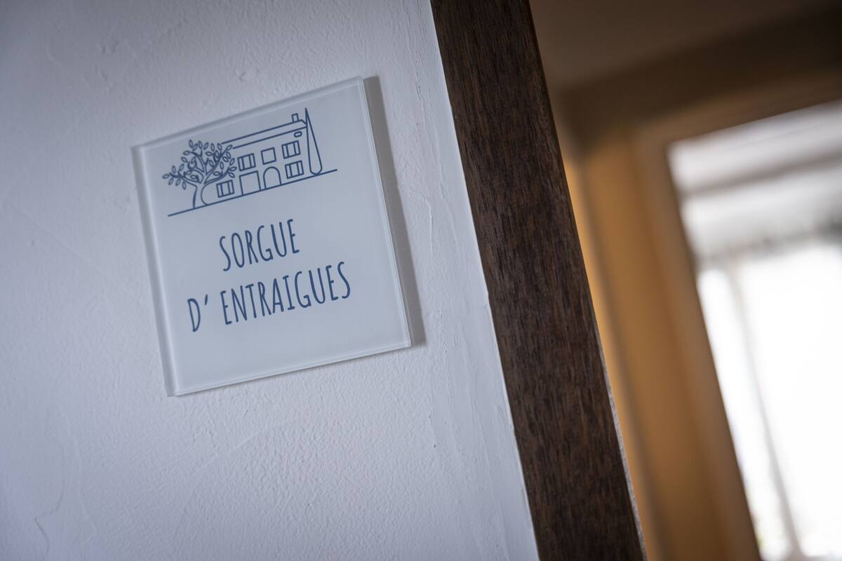 A sign with the text "SORGUE D'ENTRAIGUES" and a simple line drawing of a building.
