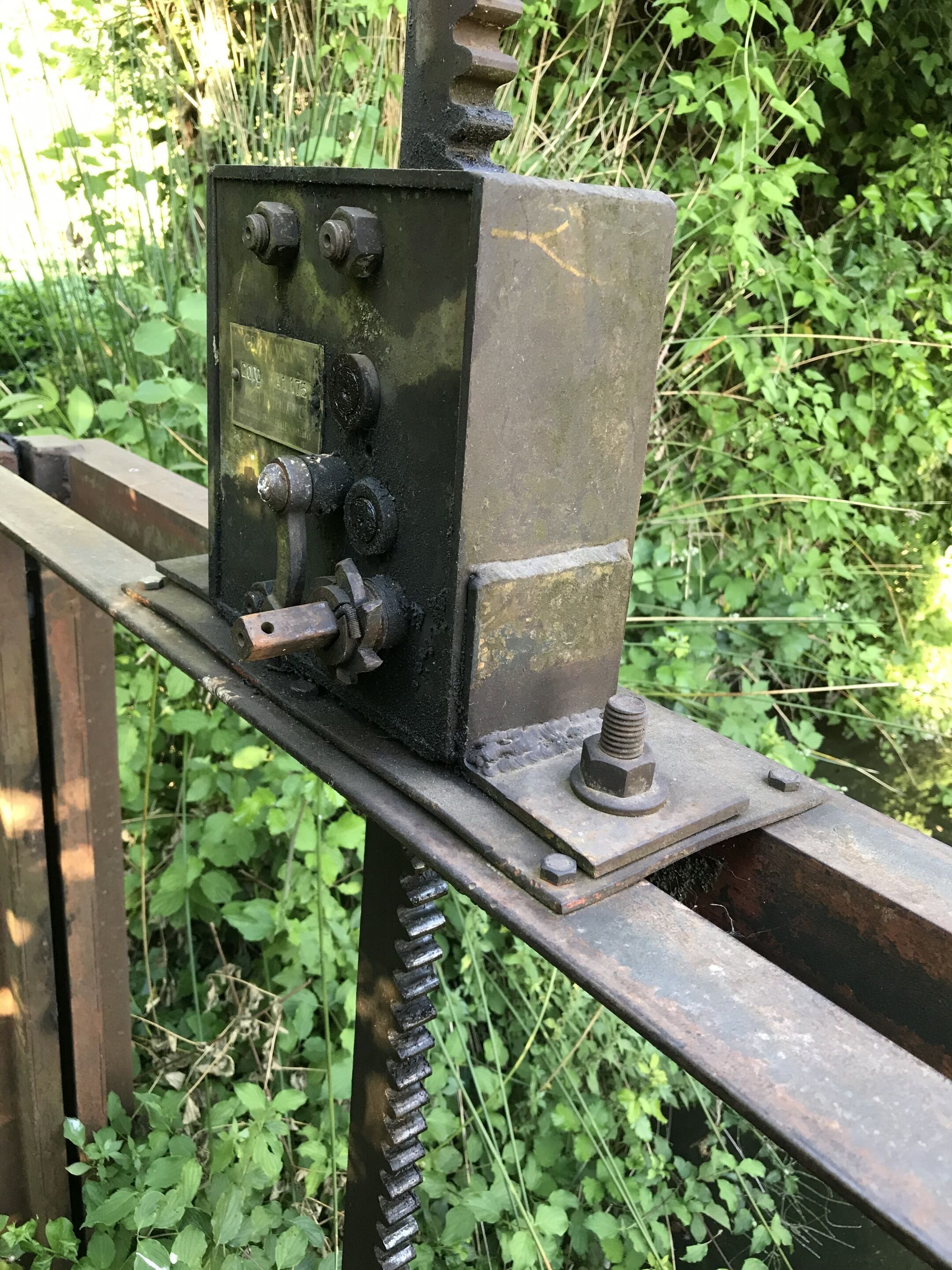 Un appareil mécanique doté de plusieurs boutons et d’une plaque métallique, fixé sur une structure métallique, avec un arrière-plan verdoyant.