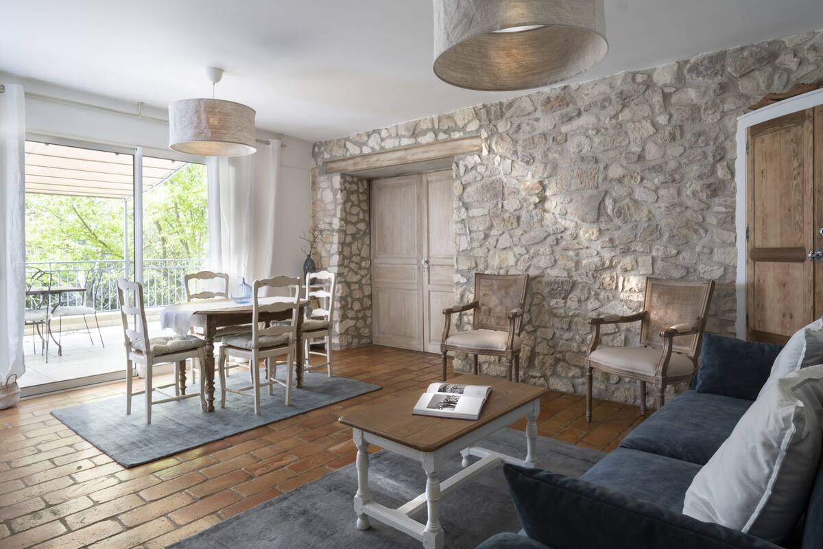 A spacious living area with a stone wall, wooden furniture, and a balcony with a view.