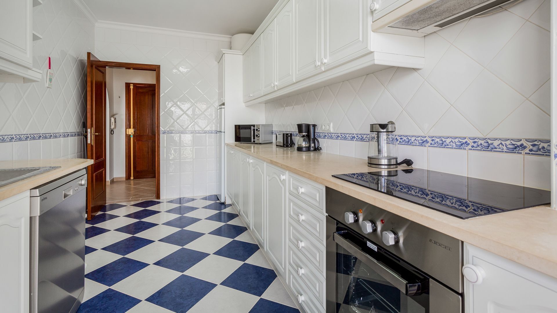 A kitchen with a checkered floor, white cabinets, a microwave, a coffee maker, and an oven.