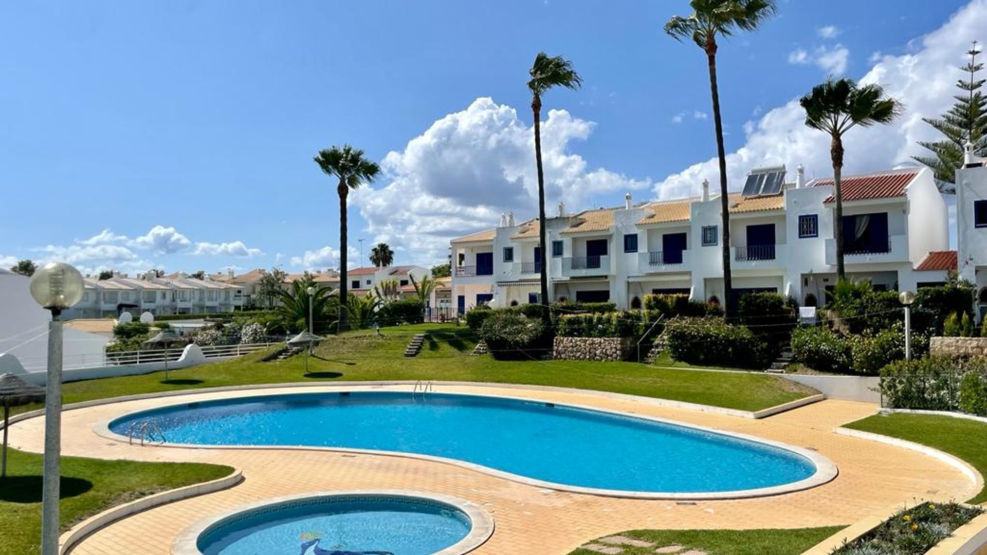 Ein Resort mit Swimmingpool, Palmen und weißen Gebäuden mit roten Dächern.