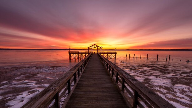 A wooden pier extending into a body of water during sunset.